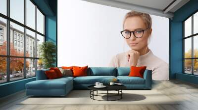 Sassy and successful good-looking accomlished female lifestyle blogger in glasses with blond hair combed holding fists under chin and looking confident at camera with daring cheeky smirk Wall mural