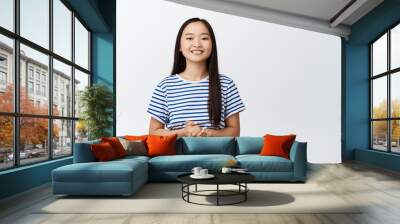 Smiling asian girl looks polite and professional, ready to help and provide assistance, stands against white background Wall mural