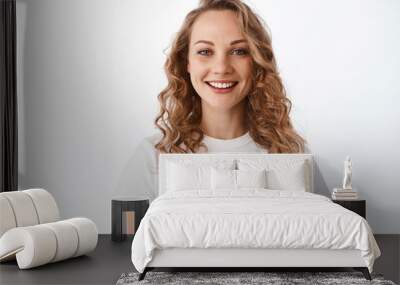 Smiling blond woman with white perfect smile and natural face, looking happy and confident at camera, standing in t-shirt against white background Wall mural