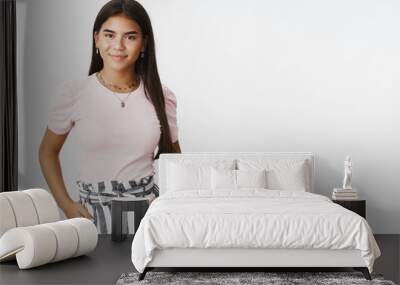 Stylish friendly-looking confident young charming teenage indian girl in striped pants and t-shirt holding hands in pockets and smiling delighted at camera as feeling assertive and carefree Wall mural