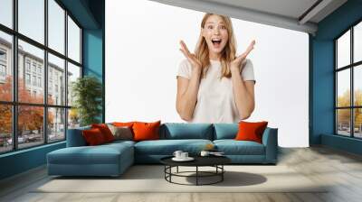 Surprised and excited blond girl screams of joy, reacting amazed and happy at promo sale, super big news, standing over white background Wall mural