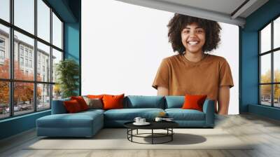 Waist-up shot of cute carefree friendly-looking African American teenage girl with afro hairstyle smiling broadly with shy and happy expression meeting new classmates over gray background Wall mural