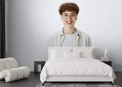 waist-up shot of optimistic and happy young handsome boy in round glasses with curly hairstyle smili Wall mural