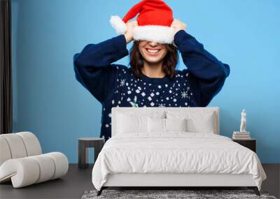 Young beautiful brunette girl in knited sweater and christmas hat smiling  over blue background. Wall mural