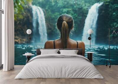 A woman in a black swimsuit swims in a serene jungle pool with two cascading waterfalls in the background, enjoying the refreshing water and natural beauty surrounding her. Wall mural