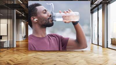 Fitness, drinking water and black man in outdoor nature for exercise, training and running with music, audio streaming service. Tired runner, sports or athlete man with water bottle for workout Wall mural