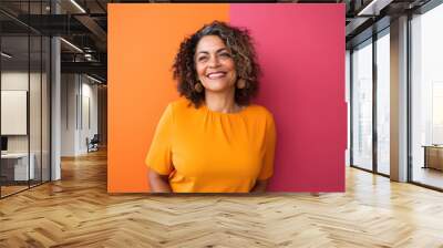 Middle aged hispanic and latina woman in her 50s smiling happily. Colorful orange and purple background, bright clothing. Wall mural