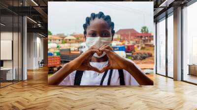 young black beautiful lady wearing a nose mask and giving a love sign with her hand Wall mural