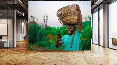 young black happy farmer carrying a basket of his farm produce on his head Wall mural