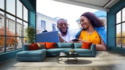 young black man and a beautiful woman sitting out, discussing and working casually on a laptop Wall mural