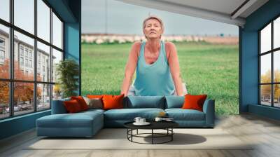 Cobra stretching, senior woman and exercise at park for workout, training and fitness. Elderly lady, yoga and flexible body outdoor on mat, grass and nature for wellness, healthy lifestyle or push up Wall mural