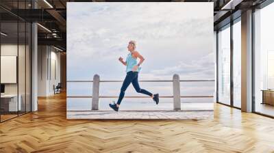 Senior woman running outdoor at on sky mockup at beach promenade for energy, health and cardio workout. Elderly female, exercise and runner at ocean for sports training, fitness and healthy marathon Wall mural