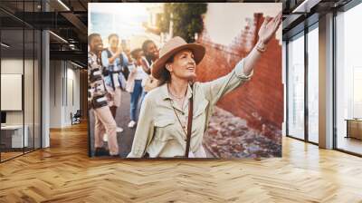 Travel, education and a teacher with students on school field trip, on urban tour. Woman, city guide and group of happy tourists, pointing at local architecture and learning on international holiday. Wall mural