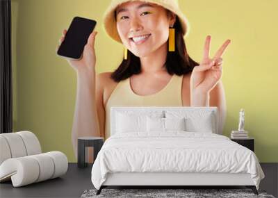 Portrait, peace sign and Asian woman with phone in studio isolated on a yellow background mockup. Makeup, fashion cellphone and smile of happy gen z female with v hand gesture and mobile smartphone. Wall mural