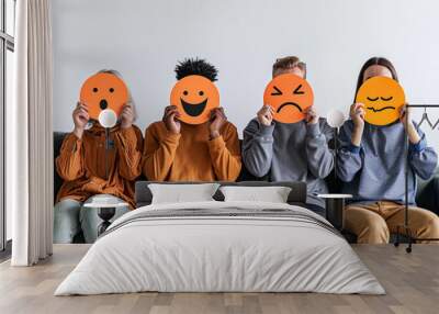 Young people are sitting on sofa and holding images with emotions in front of their faces. Expressing or trying to hide your emotions using emoticons Wall mural