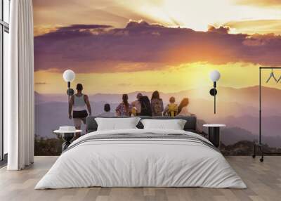 Big group of friends stands on mountain top and looks at beautiful sunset. Travel with friends concept Wall mural