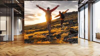 Couple hikers are walking together in sunset mountains. Two young tourists with backpacks are standing with open arms and enjoys sunset Wall mural