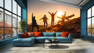 Group of happy friends are standing at mountain top and greeting sunrise or sunset above clouds Wall mural