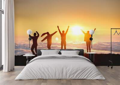 Group of happy tourists are having fun and dance at sunrise on mountain top over clouds Wall mural