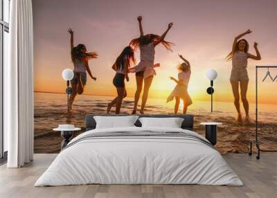 Group of happy young girls are having fun and dancing at sunset sea beach Wall mural