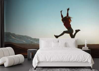 Happy girl jumps against mountains at sunset Wall mural