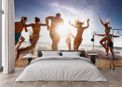 Large group of happy young tourists are having fun, runs and jumps at sunset sea beach. Tropical holidays concept Wall mural