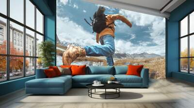 Man hiker jumps across water in mountain area Wall mural