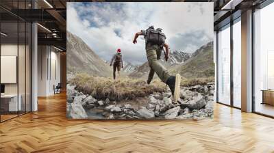 Two young hikers walks with light backpacks in mountains. Tourist jumps across the obstacle Wall mural