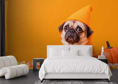 Cute pug dressed as a pumpkin sits on an orange backdrop, surrounded by colorful candy corn for a festive look. Wall mural