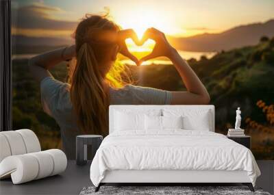 A woman making a heart with her hands in front of a sunset Wall mural