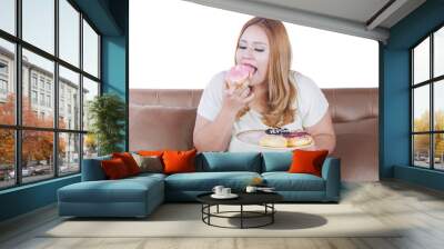 Blonde woman eats donuts on sofa Wall mural