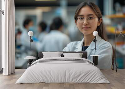 A portrait of a young female scientist in a white coat, with her team working behind her in the laboratory Wall mural