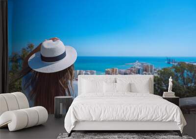 Rear view of young woman traveller with white hat standing in Gibralfaro Castle viewpoint and looking at Malaga cityscape. Summer holiday vacation in Spain Wall mural