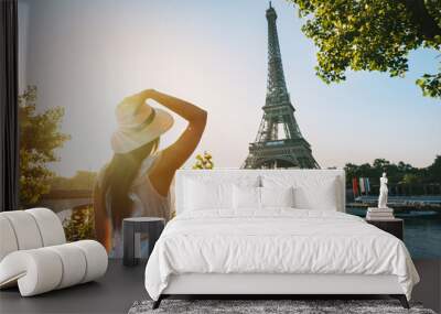 Young woman tourist in sun hat and white dress standing in front of Eiffel Tower in Paris at sunset. Travel in France, tourism concept Wall mural