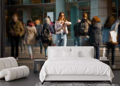 Young woman walking in the middle of crowded street and looking time at hand watches. Big city life. Wall mural