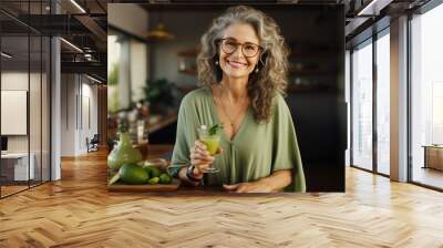 A cheerful elderly woman grinning as she holds a glass of fresh green juice. Wall mural