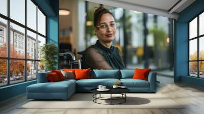 Confident woman in wheelchair, office background, casual yet professional attire. Wall mural