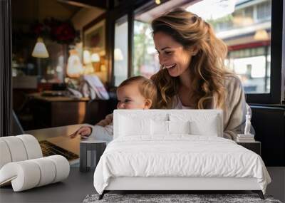 Smiling mother holding a baby on her lap while working on a laptop Wall mural