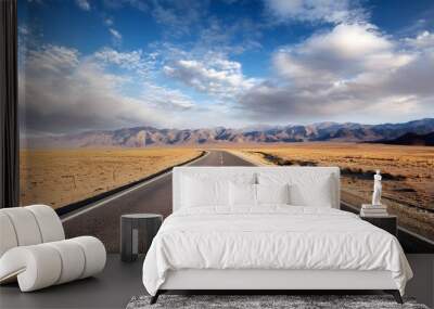 Empt Road leading trough dessert mountains and blu sky wiyh clouds in background  Wall mural