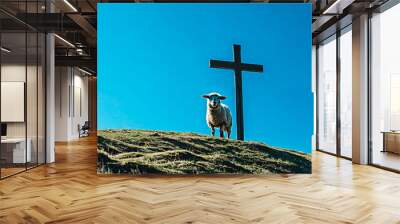 A sheep under a cross in a serene landscape with a hill under a blue sky. Religious concept. Symbolism of Church worship and salvation through faith. Wall mural