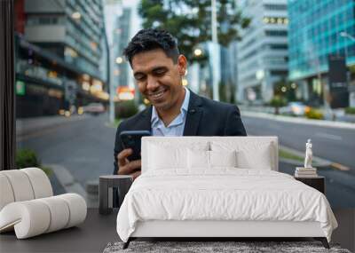 A portrait of a young smiling, happy, successful Mexican business man, executive walking outside down the street using mobile phone.  Wall mural