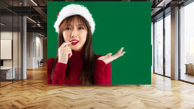 Merry Christmas, young asian woman in red sweater wearing santa hat looking camera hand pointing copy space green screen background. Wall mural