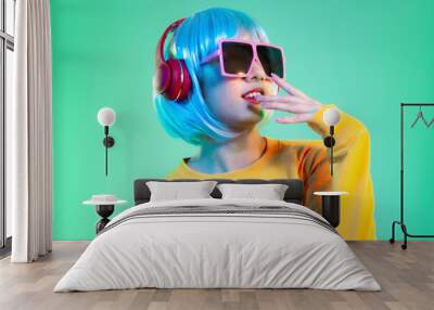 Young asian girl in yellow sweatshirt blue color shot hair style wearing red headphone and pink sunglasses listen to music posing on the green screen background. Wall mural