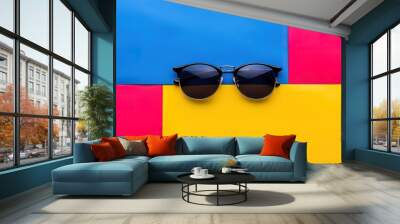 Black sunglasses on a colorful background of blue, red, and yellow. Minimalist and vibrant. Sunglasses fashion, summer style. Wall mural