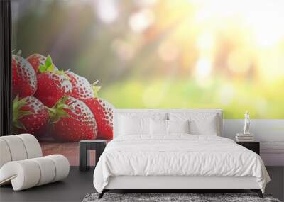 Fresh, ripe strawberries on a wooden table with a blurred background of green foliage and sunlight. A perfect image for summer, healthy eating, and fresh produce. Wall mural