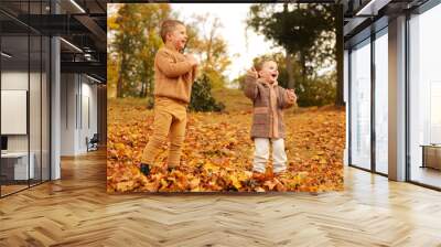 Outdoor fun in autumn. Children playing with autumn fallen leaves in park. Happy little friends. Wall mural