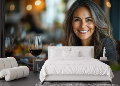 A woman with a radiant smile sitting at a welllit dining table filled with colorful, healthy dishes and wine glasses, with a soft focus on the lively background Wall mural