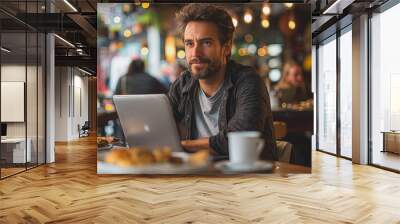 a man sitting in a restaurant using a laptop, focused on his work. Wall mural