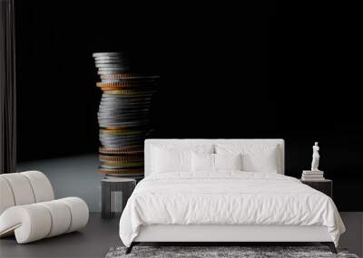 a tall stack of coins, mostly silver with a few gold and copper ones, on a white surface. The background is dark. Wall mural