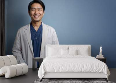 Smiling asian man physician in a white coat on blue background. Wall mural